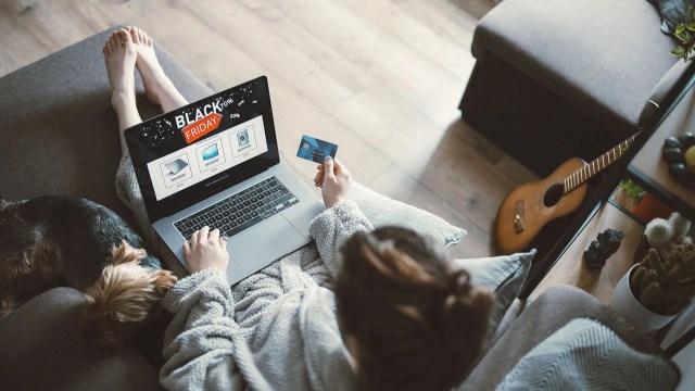 Woman relaxing on sofa at home and shopping online at Black Friday event and her dog sleeping around.