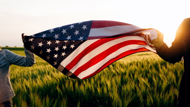 Hands holding American flag in a wheat field at sunset. Independence Day, 4th of July